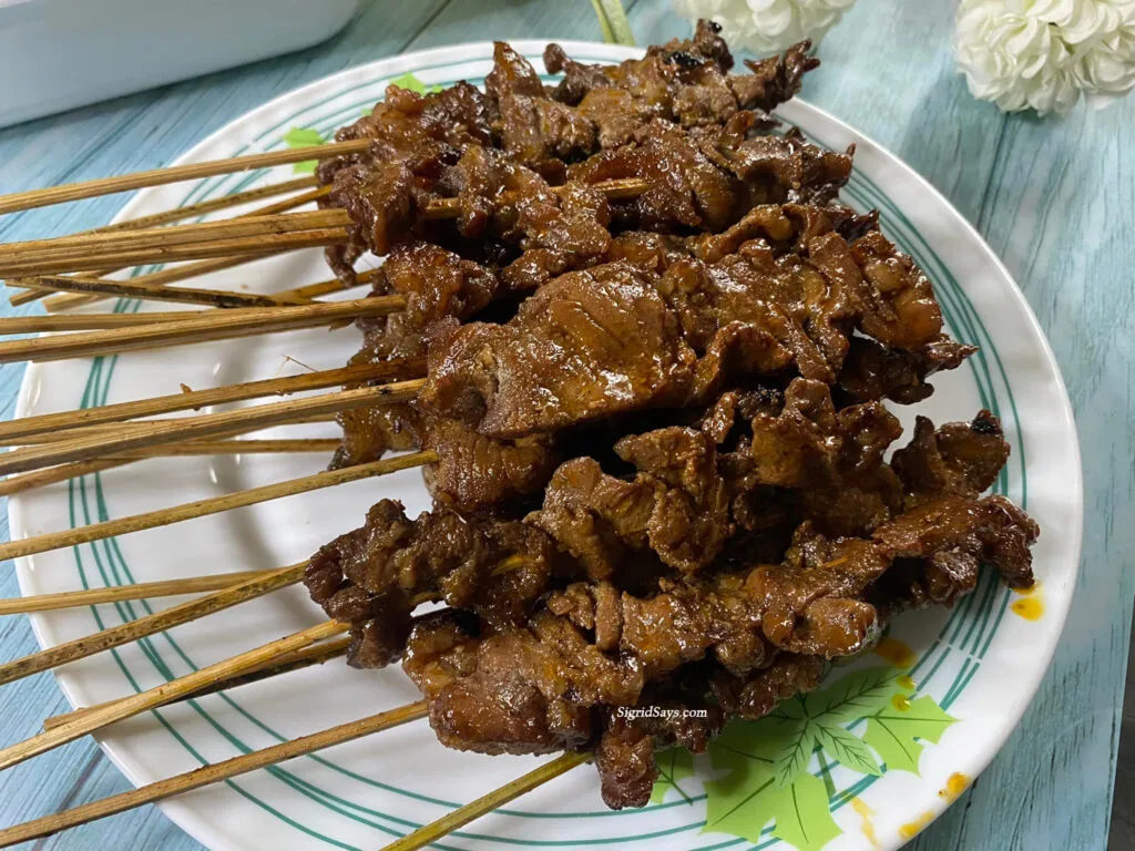 Several sticks of Lola's pork barbecue on a white plate.